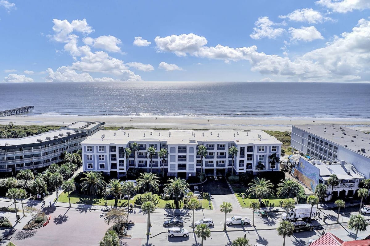 Aerial view from ocean showing wide sandy beach, pier, and colorful building mural