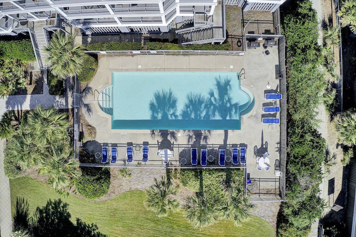 Drone directly above pool with palm shadows, blue loungers, and beach staircase