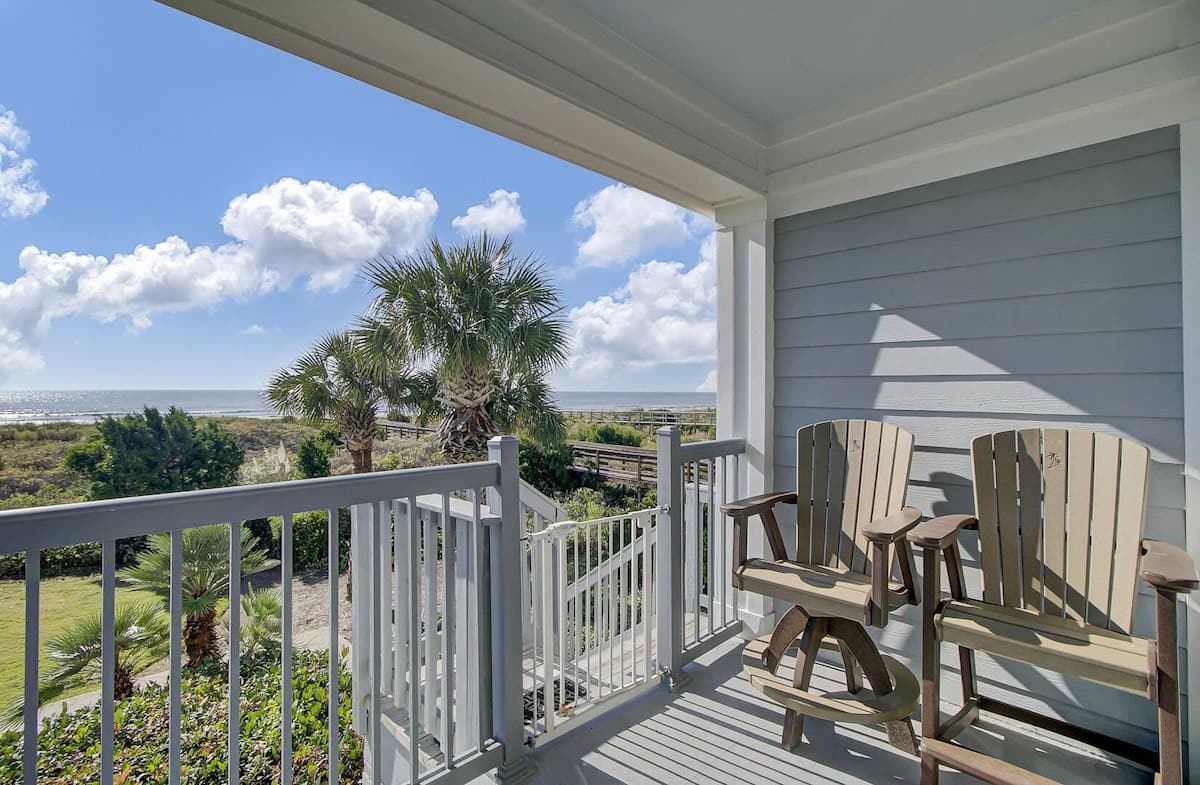 Private balcony with two Adirondack bar chairs, palm trees, and panoramic ocean view