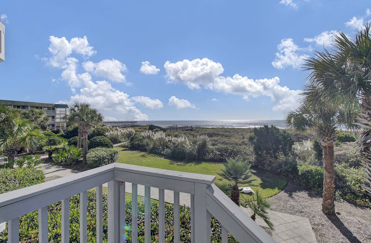 Balcony view over railing with tropical landscaping, boardwalk, and dramatic ocean clouds