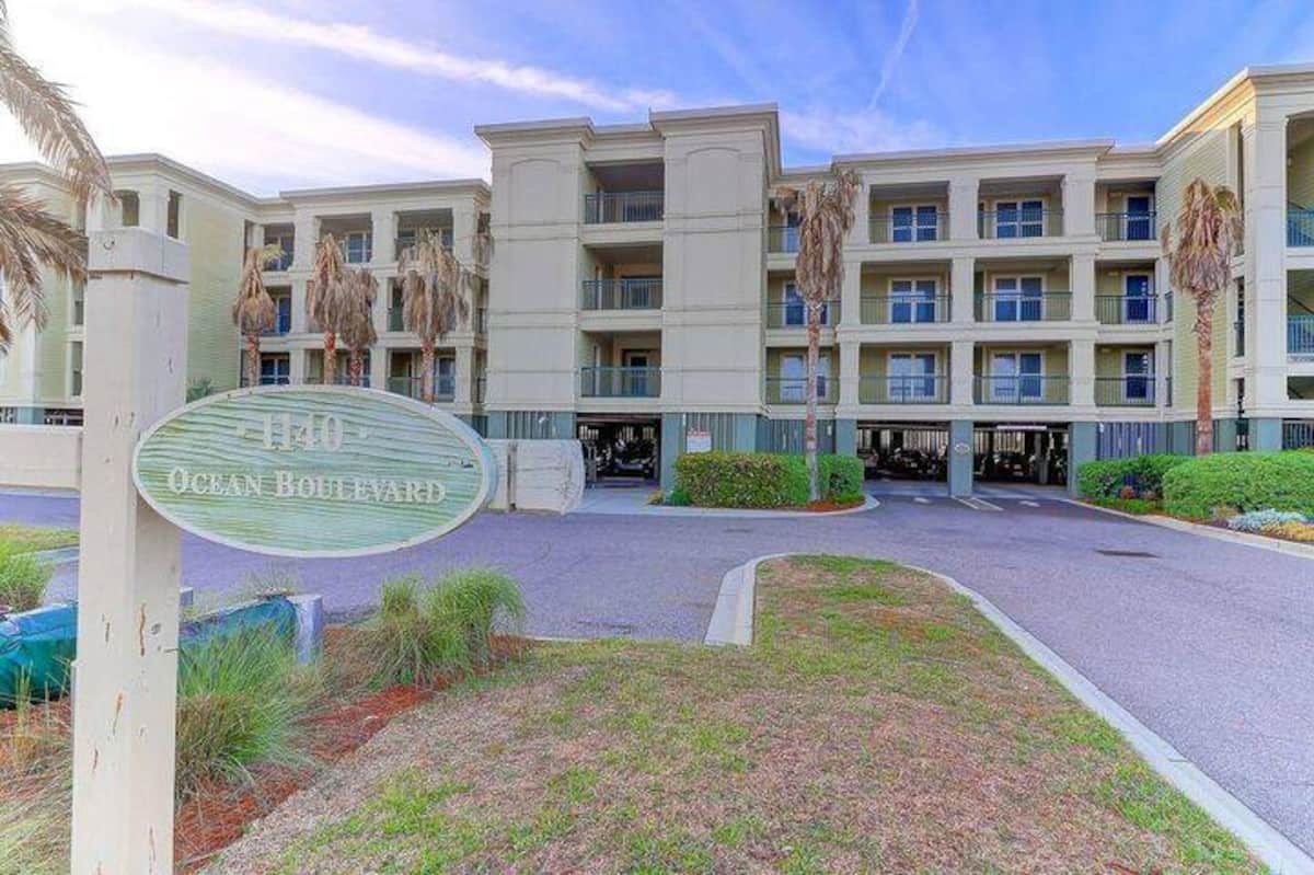 1140 Ocean Blvd front entrance with circular logo, condos, palms, and parking