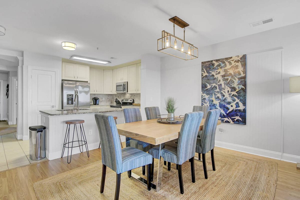 Dining area with blue-striped chairs, natural wood table, gold cage chandelier, seabird art