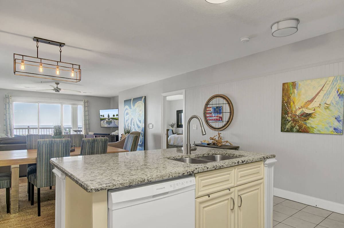 Kitchen island with dishwasher, granite counters, sailboat art, dining area visible