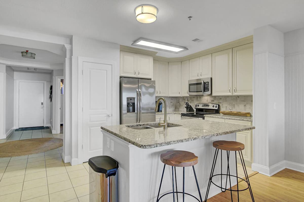 Kitchen island with granite counters, industrial bar stools, and stainless fridge