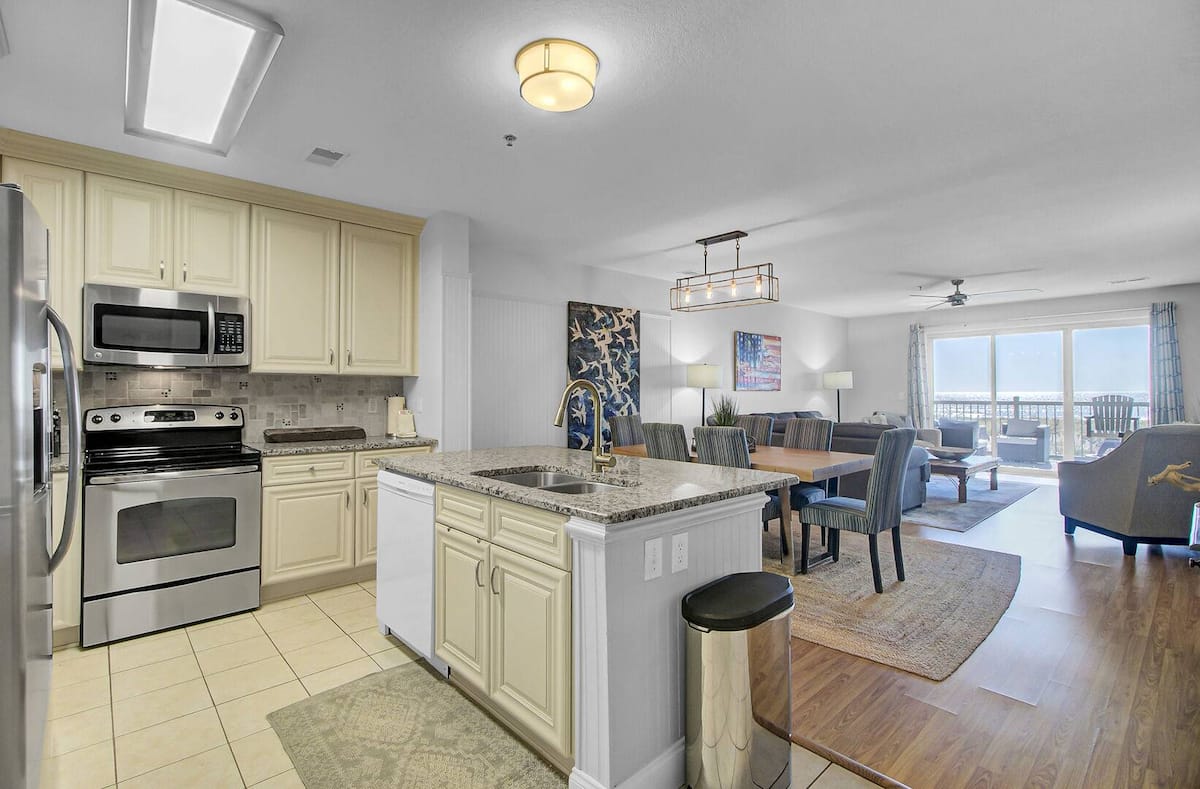 Open-concept kitchen with cream cabinets, granite island, and ocean view through living area