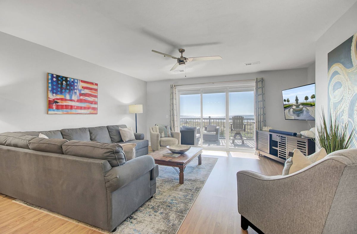 Living room with American flag canvas, L-shaped gray sectional, and open balcony doors