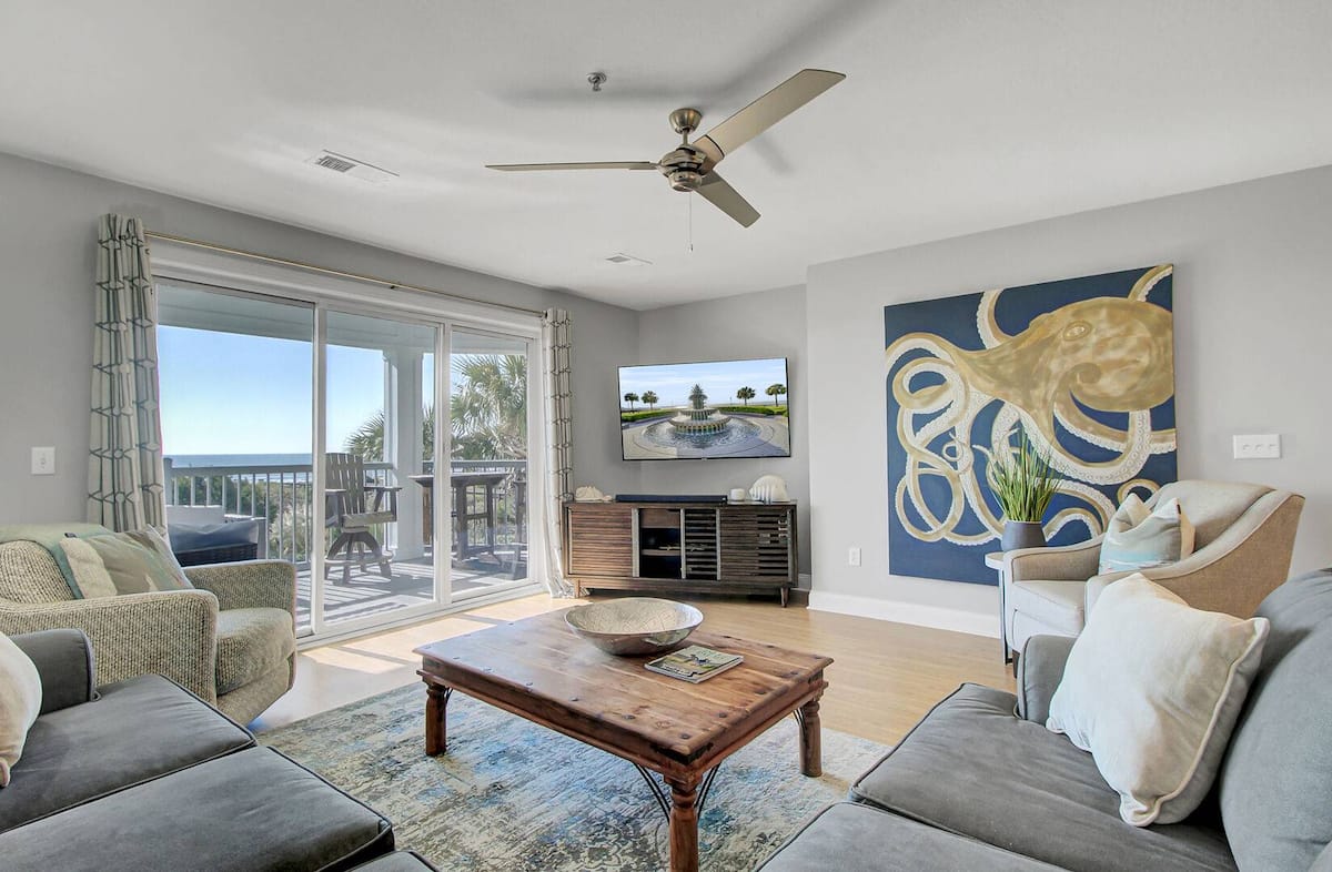 Living room with golden octopus painting, ceiling fan, rustic coffee table, and ocean balcony