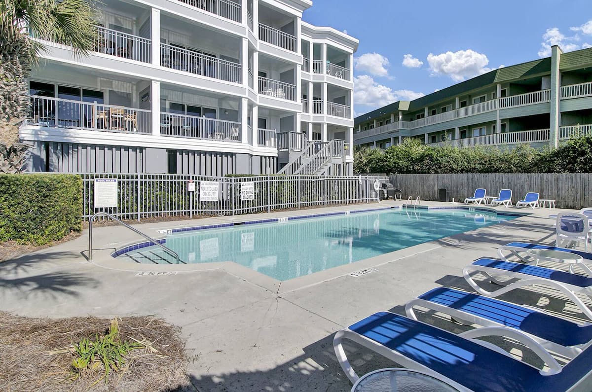 Pool with blue loungers, 1140 Ocean Blvd balconies, and palm trees