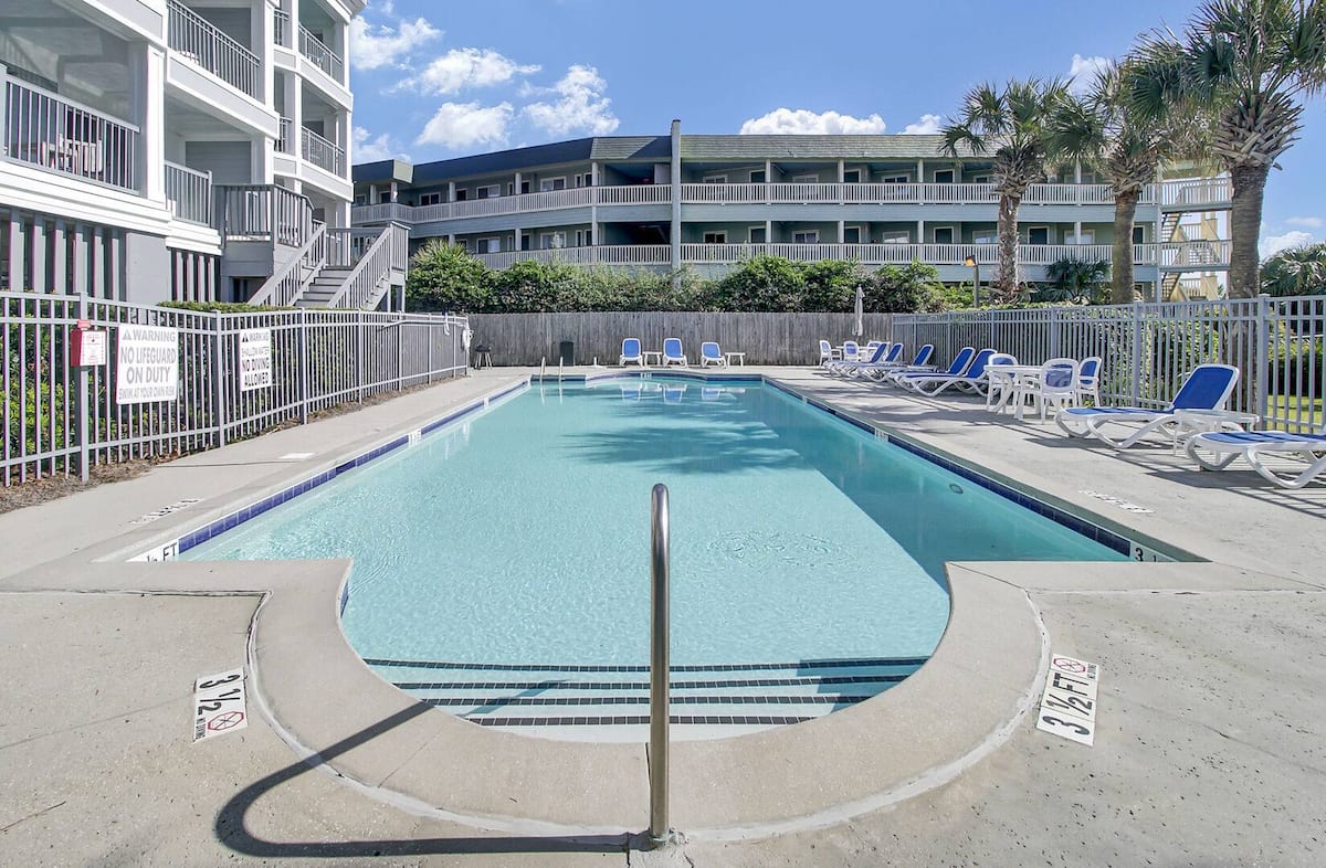Pool deck with depth markers, loungers, and condo buildings on both sides