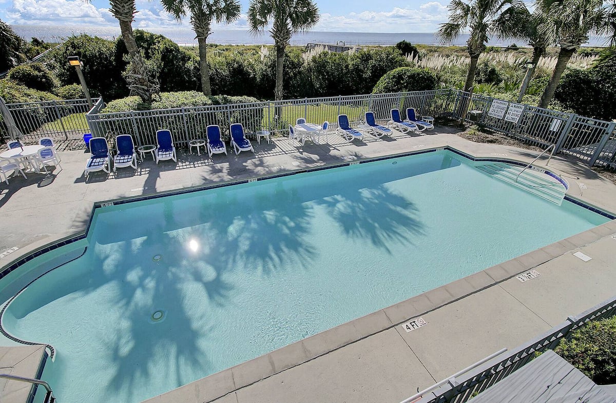 Pool view toward Atlantic with loungers, palms, and iron fence with ocean beyond