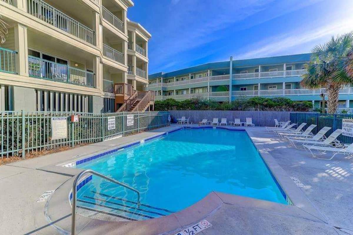 Pool at ground level with turquoise water, white loungers, and condo buildings