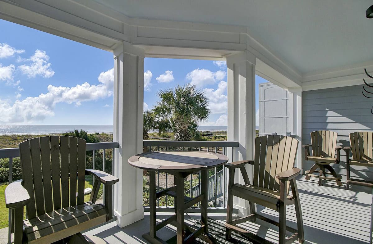 Screened porch dining area with Adirondack chairs around table, overlooking ocean