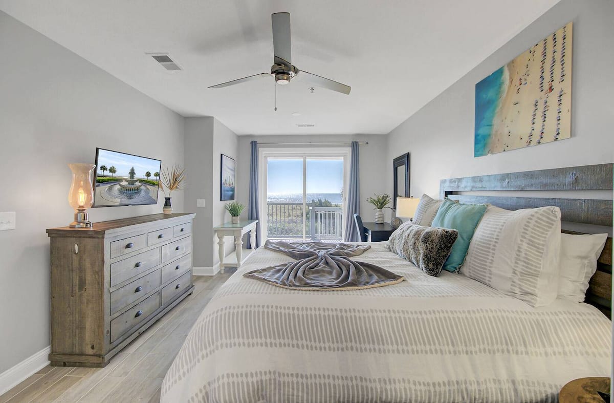 Primary bedroom with weathered wood dresser, TV, and balcony ocean view
