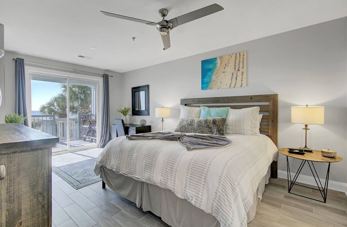 Primary bedroom with king bed, rustic headboard, ocean view through balcony door, beach art