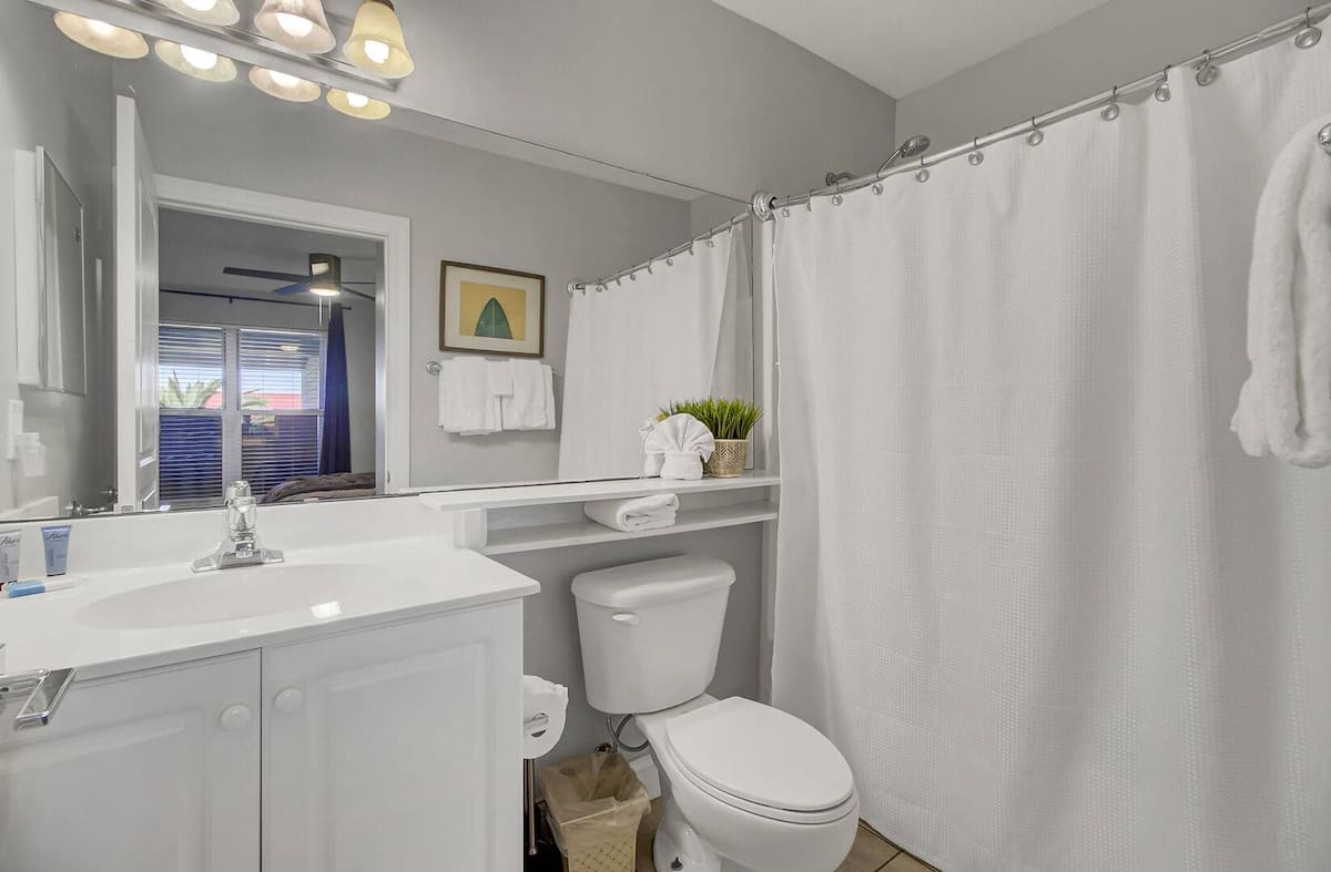 Second bathroom with white vanity, shower-tub combo, and decorative greenery