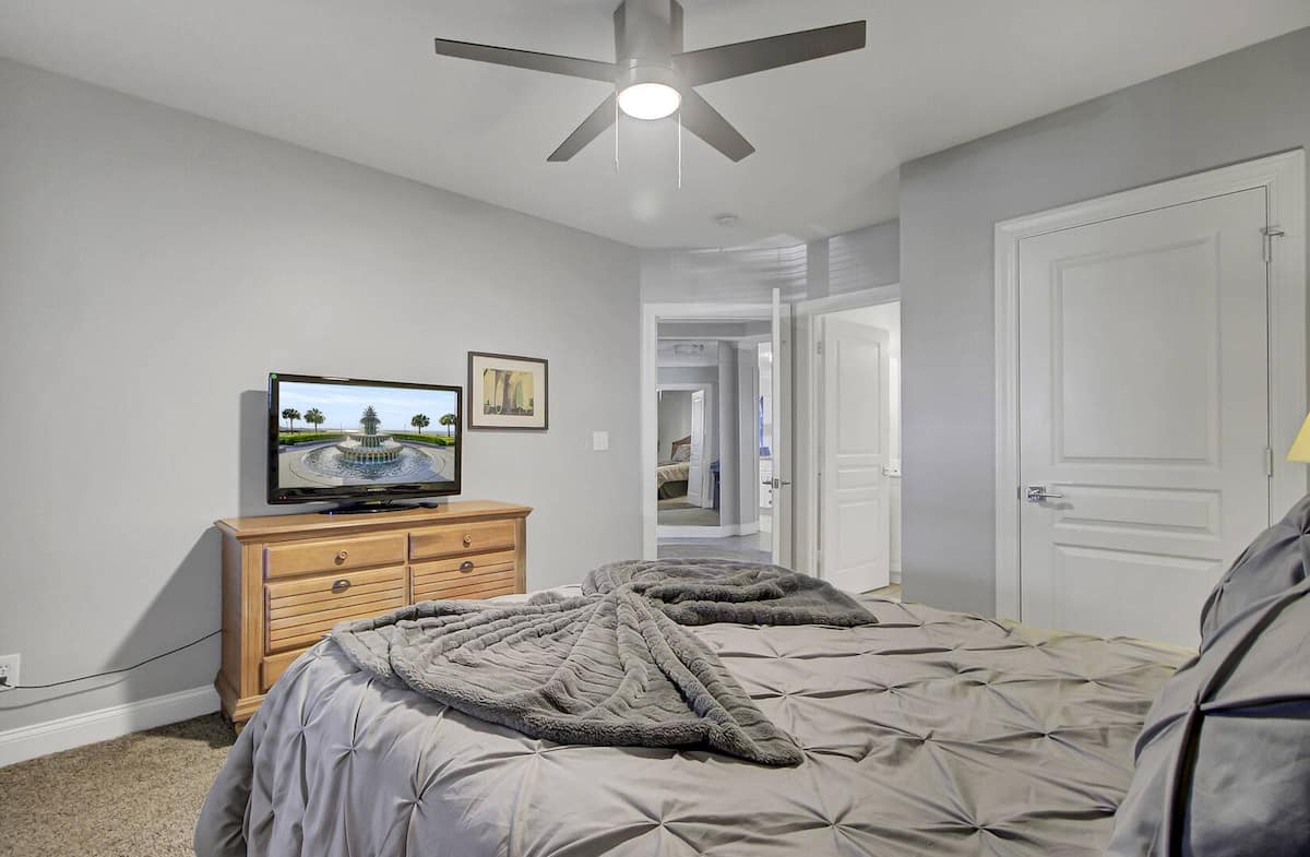 Second bedroom alternate — queen bed, TV on oak dresser, and hallway view