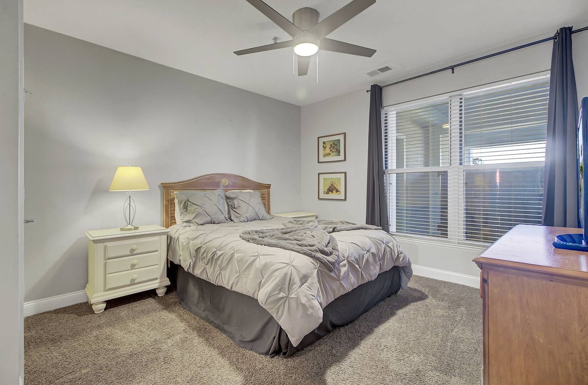 Second bedroom with queen bed, traditional headboard, gray comforter, and ceiling fan