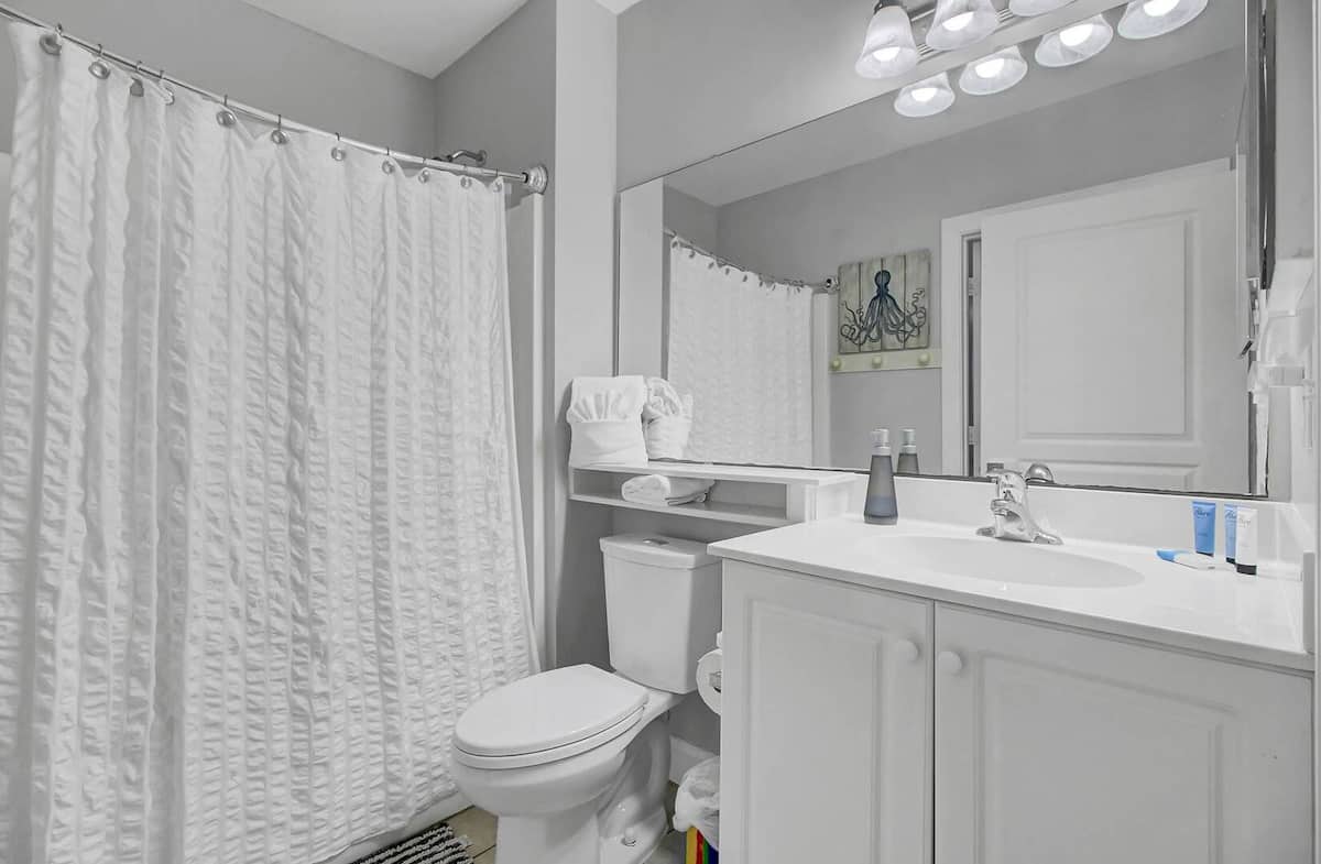 Third bathroom with white vanity, shower-tub combo, and octopus art on shelf