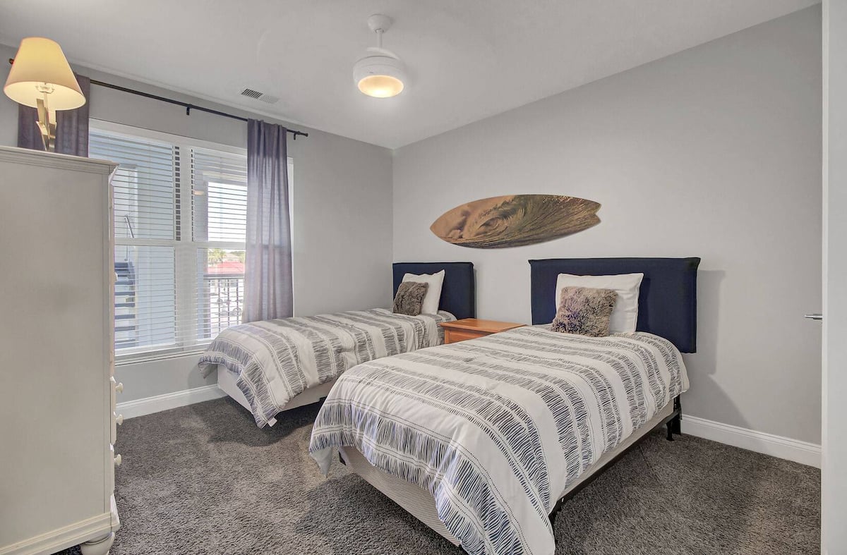 Third bedroom with twin beds, navy headboards, striped bedding, and decorative surfboard
