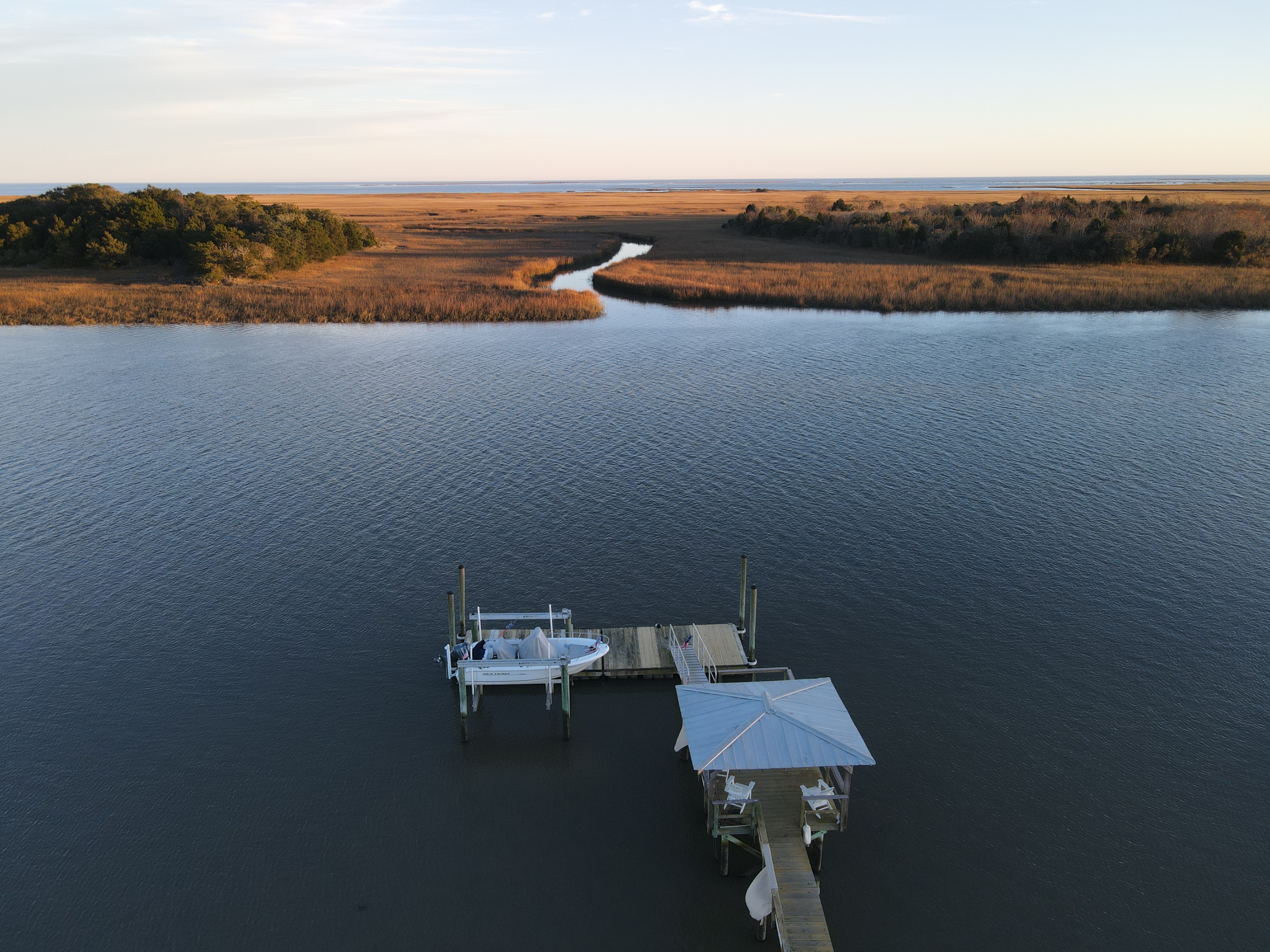 Aerial drone view of private dock stretching into Graham Creek at golden hour — boat lift, covered gazebo, and Intracoastal marsh as far as the eye can see